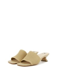 Mules beige con tacco, realizzati in un tessuto a coste, con punta aperta e un tacco scultoreo a forma triangolare. Suola liscia e stile minimalista.