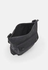 Černá crossbody taška s otevřeným horním zipem, přední kapsou na klopě se dvěma patentkami a nastavitelným popruhem.