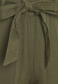 Olijfgroen stof met een visgraatpatroon, voorzien van een gestrikt riem en geplooide details. Zachte textuur met verticale lijnen.