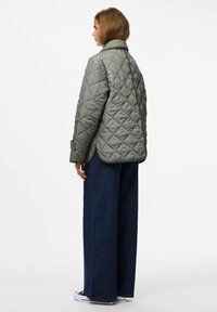 Giacca trapuntata verde oliva con colletto alto, caratterizzata da un motivo a rombi e una vestibilità rilassata, abbinata a pantaloni in denim scuri a gamba larga.