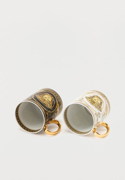 Δύο περίτεχνα κεραμικά φλυτζάνια, ένα μαύρο και ένα λευκό, με χρυσές λαβές και κλασικά σχέδια με χρυσή κεφαλή Μέδουσας, που είναι τοποθετημένα πλαγίως.