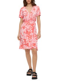 Rosa Blumenkleid mit kurzen Ärmeln, tailliertem Schnitt, volantriemen und weichem Stoff. Kombiniert mit schwarzen Plateausandalen.