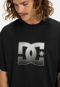 Black cotton t-shirt featuring a bold, silver graphic logo with a dotted pattern and star detail on the front. Short sleeves and crew neck design.