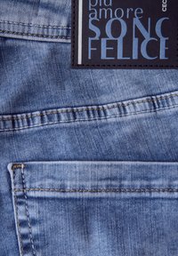 Ljusblå denimtyg med en texturerad yta, utrustad med en svart etikett med vit och blå text som är sydd på bakfickan.