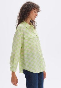 Light green button-up shirt with a wavy white pattern, featuring two chest pockets and long sleeves, made from a smooth fabric.