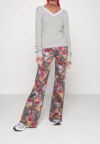 Grå kabelstickad tröja med V-ringning; blommönstrade utsvängda byxor i livfulla färger; modellen bär silverfärgade sneakers.