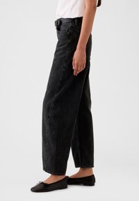 Musta, korkeavyötäröinen ja väljälahkeinen farkku, jossa on hienovarainen tekstuuri. Yhdistetty mustiin, litteäpohjaisiin kenkiin, joissa on rusetti, tyylikkäästi viimeistelty vyöllä.