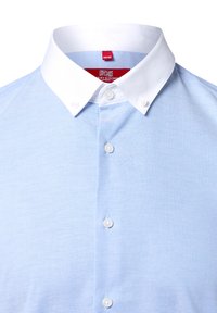 Camicia in cotone celeste chiaro con colletto bianco a punta, dotata di chiusure a bottone sul davanti e una texture liscia. Etichetta visibile all'interno del colletto.