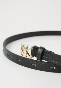 Curea din piele neagră cu model embosat și cataramă geometrică aurie în formă de pătrat pe fundal alb.