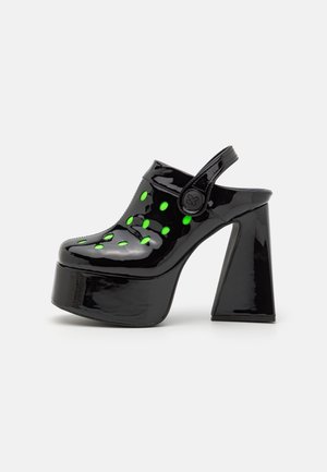 Sabots à plateforme en cuir verni noir avec un talon carré haut, ornés d'accents circulaires verts et d'une sangle arrière pour un maintien sûr.