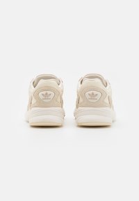 Beige mockasin- och lädersportskor med en vadderad krage, utrustade med en lätt sula och en präglad logotyp på hälen.