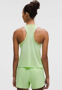 Canottiera atletica verde chiaro con design racerback e dettagli riflettenti. Il materiale appare leggero e traspirante, abbinato a pantaloni corti coordinati.