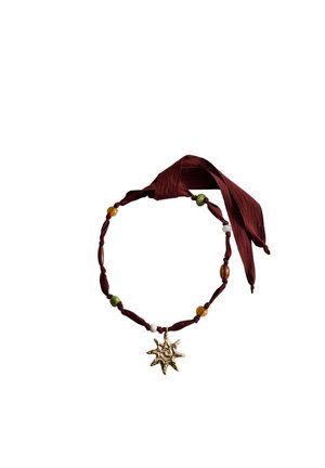 Collier ras-du-cou en tissu avec des perles vertes, ambrées et blanches, doté d'un pendentif doré en forme de soleil et attaché avec un ruban rouge foncé.