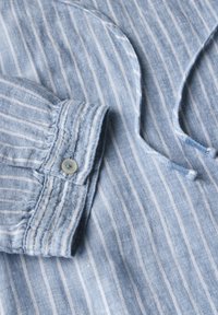 Chemise rayée bleu clair avec des poignets boutonnés, en tissu doux, au design décontracté et avec des détails de lien au niveau du décolleté.