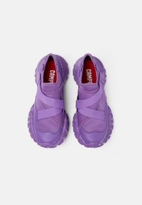 Scarpe slip-on viola con cinturini elastici, bordi texture e suole in gomma con forma arrotondata e marchio rosso all'interno.