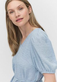 Ljusblå, texturerad klänning med puffärmar och V-halsringning. Har ett dragsko i midjan och ett vävt mönster genom hela tyget.