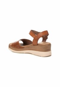 Sandalias de cuña de cuero marrón con patrones florales recortados, una banda ancha y una suela texturizada beige con un leve tacón.