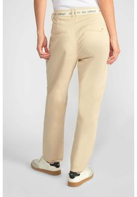 Beige broek met een gestructureerde afwerking, voorzien van een logo tailleband, achterzakken en een recht model, gecombineerd met witte sneakers.