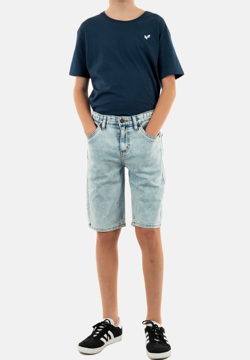 Dunkelblaues Baumwoll-T-Shirt mit einem weißen Logo, kombiniert mit hellblauen Jeansshorts und schwarzen Sneakers mit weißen Streifen. Sichtbare genähte Taschen.
