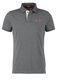 Šedé polo tričko s krátkými rukávy, s třemi knoflíky a bílým límečkem. Na levé části hrudi je umístěno malé červené logo ptáčka.