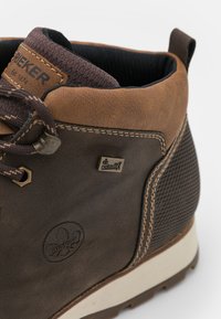 Brown leather boot with textured upper, knit collar, metal logo accent, and contrasting rubber sole. Features stitching and mesh paneling.