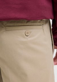 Pantalones de algodón beige con un bolsillo trasero con cierre de botón, complementados por un suéter de punto texturizado color burdeos arriba.