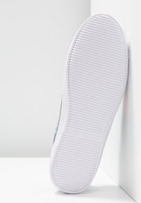 Semelle de chaussure blanche avec de fines rainures horizontales et un motif d'adhérence texturé sur un fond blanc uni aux coins nets.