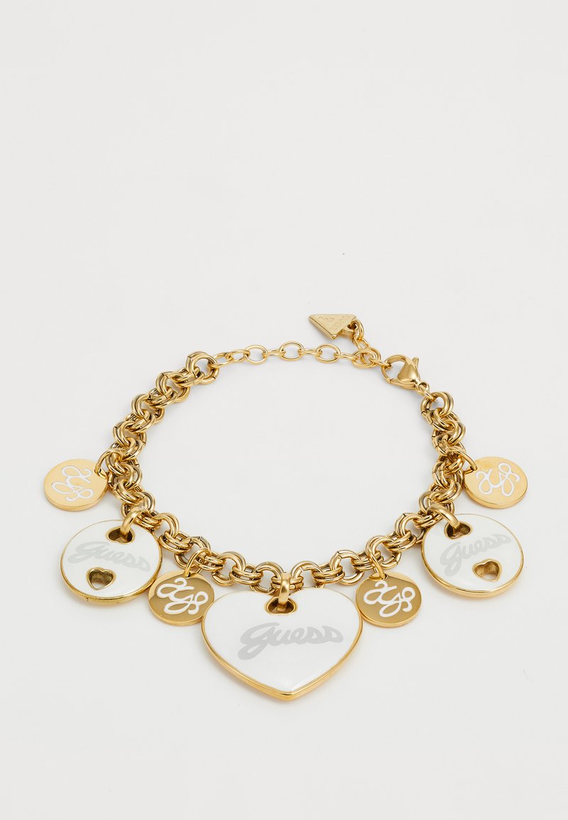 Guldtonad armband med stora hjärtan och cirkulära berlocker, vissa med vit emalj, graverade logotyper och ett lobsterkläpps-lås.
