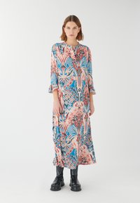 Blumenlangkleid mit einem Muster in Pink, Blau und Grün, runder Ausschnitt und ausgestellten Ärmeln, kombiniert mit schwarzen Plateaustiefeln.