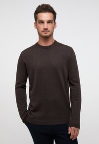 Brauner Pullover mit Rundhalsausschnitt aus weichem Strickstoff, mit langen Ärmeln und geripptem Saum, kombiniert mit dunklen Hosen.