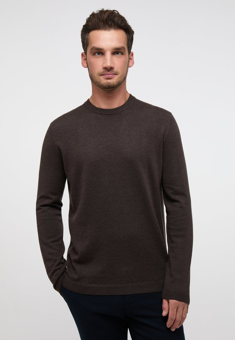 Brauner Pullover mit Rundhalsausschnitt aus weichem Strickstoff, mit langen Ärmeln und geripptem Saum, kombiniert mit dunklen Hosen.