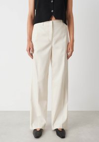 Wijdvallende, crèmekleurige broeken van katoen, met een trekking rits, riemlussen en een minimalistisch design zonder zichtbare patronen.