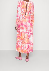 Robe à manches longues tie-dye dans des tons rose et orange, avec un dos échancré et un ourlet à volants superposés. Tissu lisse, longueur jusqu'aux chevilles.