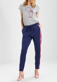 Camiseta gris con gráfico de spray y nube; pantalones jogger azul marino con acentos florales rojos a los lados; tela suave; silueta ajustada; combinados con tacones rosas.