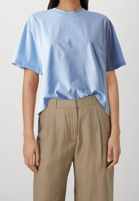 Ljusblå bomulls t-shirt med kort ärm, rund halsringning och avslappnad passform. Matchas med beigefärgade byxor med en mjuk textur och veck.
