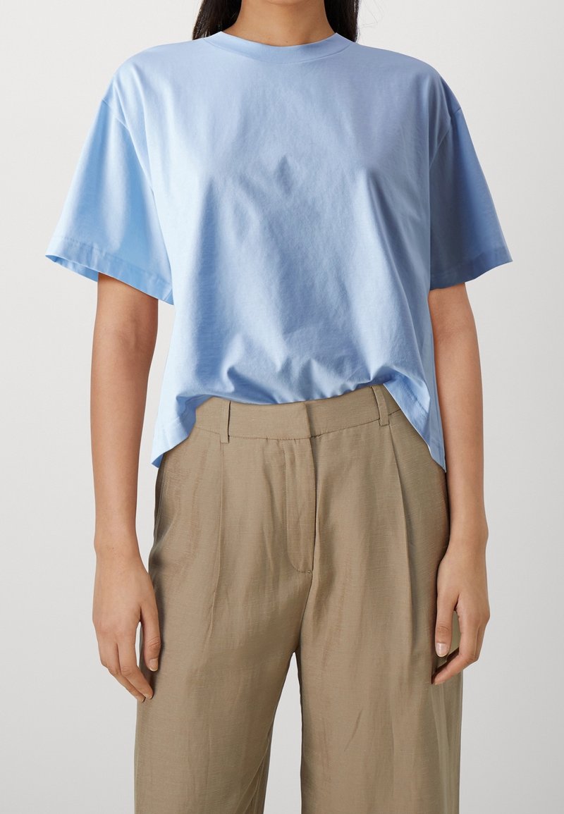 Ljusblå bomulls t-shirt med kort ärm, rund halsringning och avslappnad passform. Matchas med beigefärgade byxor med en mjuk textur och veck.