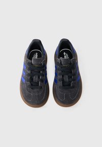 Pár tmavosivých tenisiek Adidas s modrými pruhmi, čiernymi šnúrkami a hnedými členitými podrážkami na bielom pozadí.