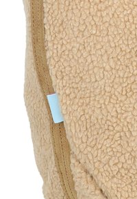 Tessuto in pile color marrone con una superficie testurizzata, dotato di una cerniera lungo il lato e un piccolo etichetta blu che contrasta con il materiale.