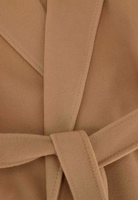 Tanwrap coat med mjuk, borstad textur, bred krage och en knytning i midjan. Tydlig sömnad syns längs kanterna.