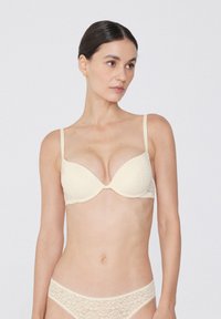 Beige Spitzen-BH mit vorgeformten Cups und verstellbaren Trägern, der mit floralem Muster und nahtlosem Design für zusätzlichen Komfort versehen ist.