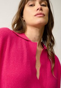 Helles, pinkes, strukturiertes Sweatshirt mit Kragen und tiefem V-Ausschnitt, ausgestattet mit geripptem Stoff und lockerer Passform.