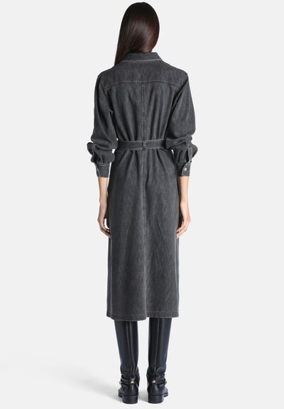 Femme aux longs cheveux portant une robe midi gris foncé à manches longues avec ceinture et des bottes noires montantes, vue de dos.