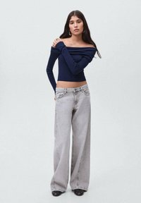 Námořnický top bez ramínek s žebrovaným vzorem spárovaný s vysokým pasem světlými šedými kalhotami s širokými nohavicemi. Kalhoty mají klasický styl s pěti kapsami.