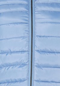 Lyseblå pufferjakke med quiltet design, der har en central lynlås og en glat, skinnende stofoverflade.