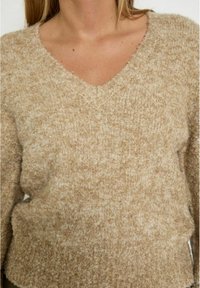 Beige, pluizig gebreid sweater met een V-halsontwerp, gestructureerd oppervlak en een ontspannen pasvorm. Ideaal voor het lagen of casual dragen.
