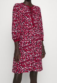 Puna mekko, jossa on leopardikuvio valkoisena, mustana ja vaaleansinisenä. Mekossa on pyöreä pääntie, jossa on nauha, ja kolmanneksen pituisten hihansuiden. 