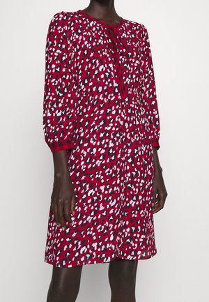 Röd klänning med leopardtryck i vitt, svart och ljusblått. Har en rund halsringning med slips och ärmar i trekvarts längd.