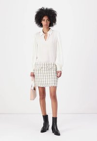 Blusa blanca con escote en V y mangas largas con pliegues, combinada con una falda de tweed ajustada en color crema con hilos multicolores. Botines negros hasta el tobillo.