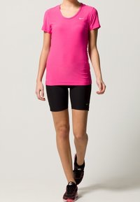 Lyserød kortærmet atletisk skjorte fremstillet af letvægtsmateriale, parret med sorte tætsiddende shorts og sorte atletiksko. Nike-logoer til stede.