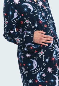 Marineblauw pyjamahemd met een hemels patroon van manen, sterren en harten in wit, rood en blauw. Met knoopsluiting aan de voorkant en contrasterende boorden.